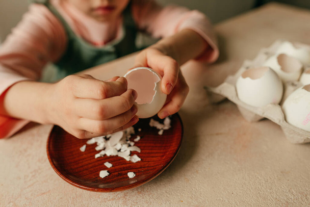 Close up of little girl peel an egg for planting seeds in a eggshells. Home gardening with kids on the kitchen windowsill. Selective focus. - Foto, immagini