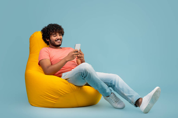 Tyylikäs hindu kaveri istuu papu pussi, käyttäen matkapuhelin - Valokuva, kuva