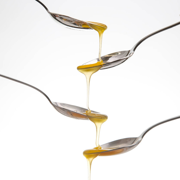 Fresh flower honey drips from a spoon into a spoon on a white background. Organic vitamin food. - Fotó, kép