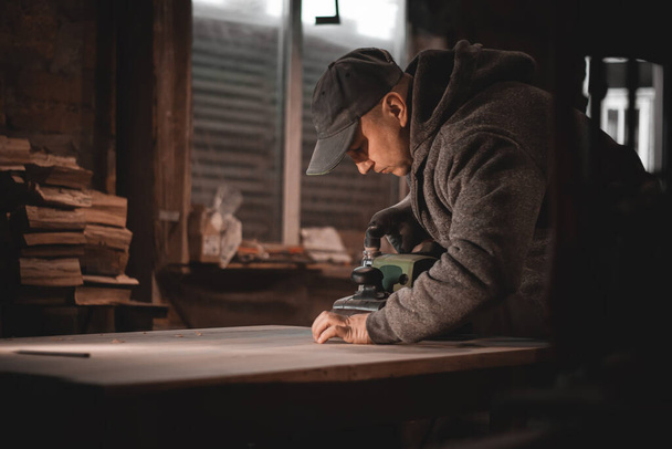 A carpenter works in a workshop. Joiner's grinders, furniture manufacturing. A carpenter is grinding a wooden part with an electric sander. - Photo, Image