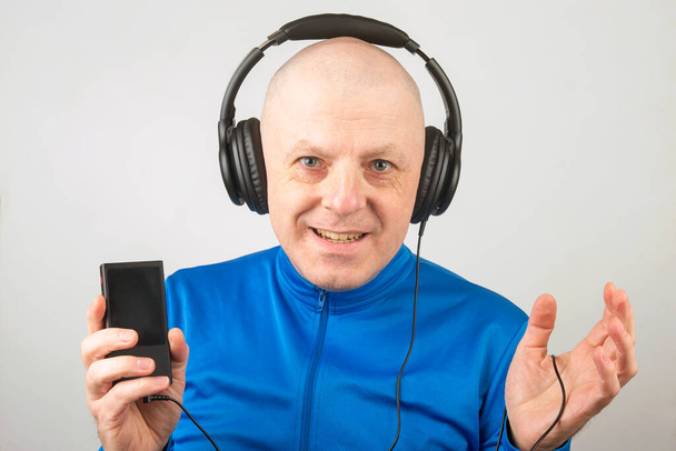 χαμογελαστός άνθρωπος με ακουστικά και ψηφιακή φορητή συσκευή αναπαραγωγής στο χέρι χαλαρώνει ακούγοντας την αγαπημένη του μουσική - Φωτογραφία, εικόνα