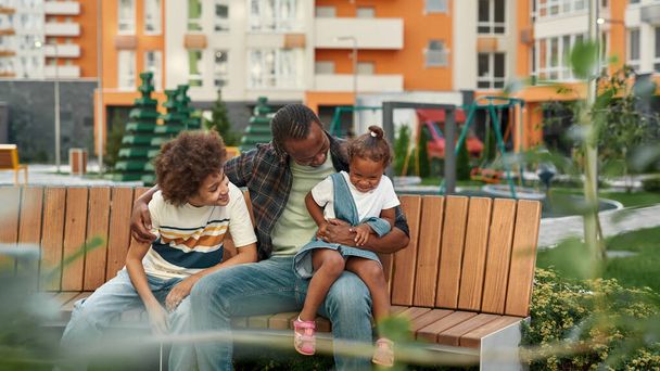 Happy black family resting on wooden bench in yard - Фото, изображение