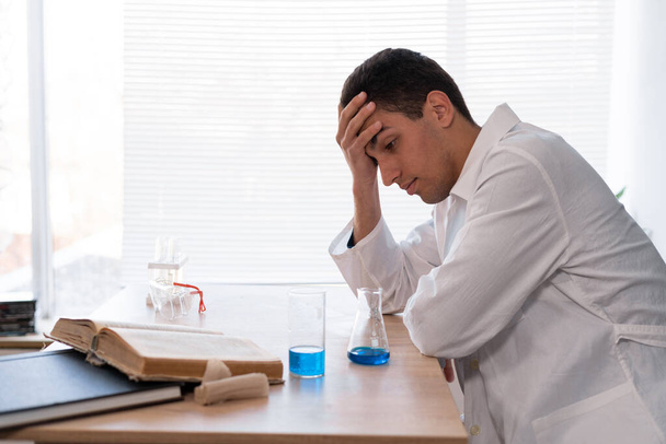 Stressed out scientist researcher feeling tired while worrying about a problem in chemistry lab. Young arab studying chemistry in a laboratory room, school chemistry teacher, results of the experiment - Фото, зображення