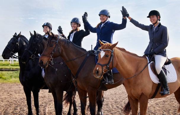 We did it. Cropped shot of a group of attractive young female jockeys high-fiving while sitting on their horses backs. - Photo, Image