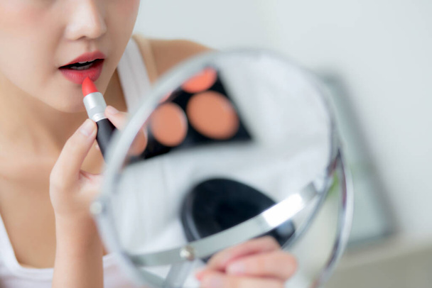 Hermosa mujer asiática joven aplicando lápiz labial rojo en la boca, chica de belleza mirando facial en el espejo para maquillaje cosmético con elegancia de labios, maquillaje con sexy de mujer, cuidado de la piel y concepto de salud. - Foto, Imagen