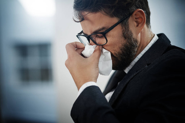 Its hard being productive when youre feeling under the weather. Shot of a young businessman blowing his nose in an office. - Foto, Imagem