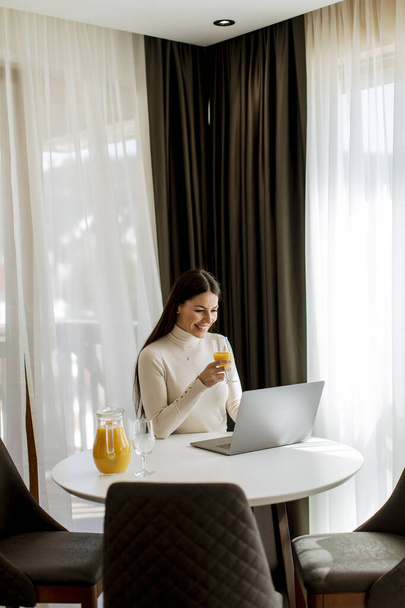 Young woman using a laptop computer and drinking healthy orange juice in the room - Fotografie, Obrázek