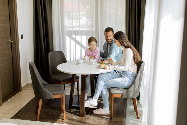 Ευτυχισμένη νεαρή οικογένεια τρώνε κέικ και πίνουν τσάι μαζί στο δωμάτιο - Φωτογραφία, εικόνα