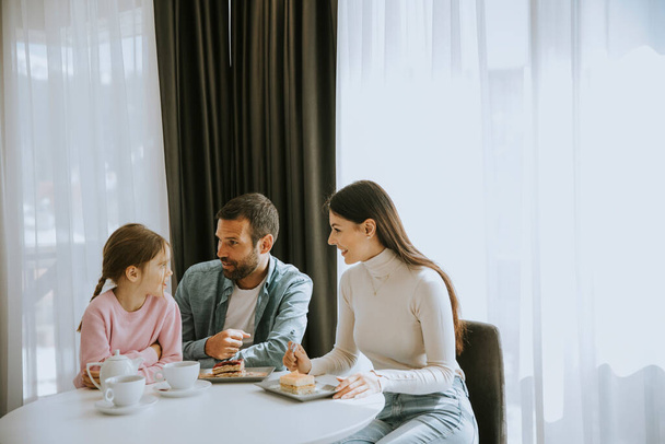 Fröhliche junge Familie isst gemeinsam Kuchen und trinkt Tee auf dem Zimmer - Foto, Bild