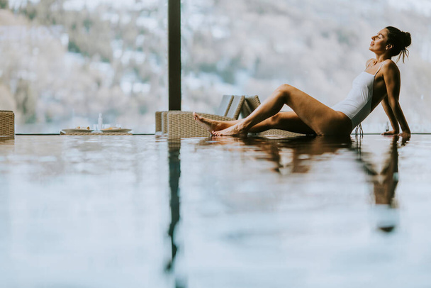 Mujer joven y bonita relajándose en la piscina de la piscina infinita en invierno - Foto, imagen