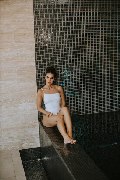 Pretty young woman relaxing on the poolside of indoor swimming pool - Foto, Imagen