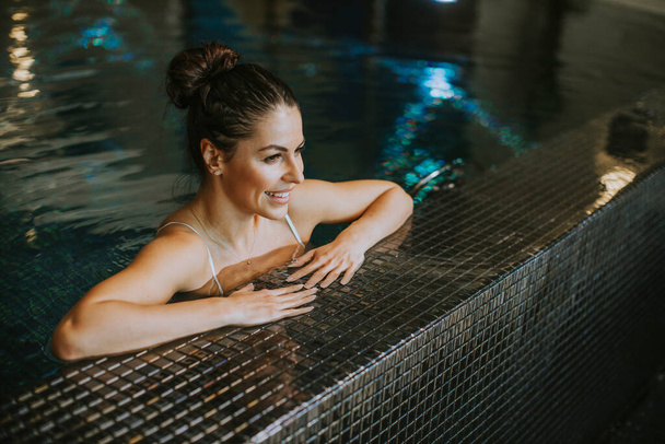 Pretty young woman relaxing on the poolside of indoor swimming pool - Foto, Imagen