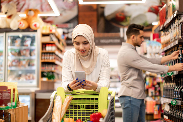 Medio Oriente Lady compras comestibles usando teléfono caminando en supermercado - Foto, Imagen