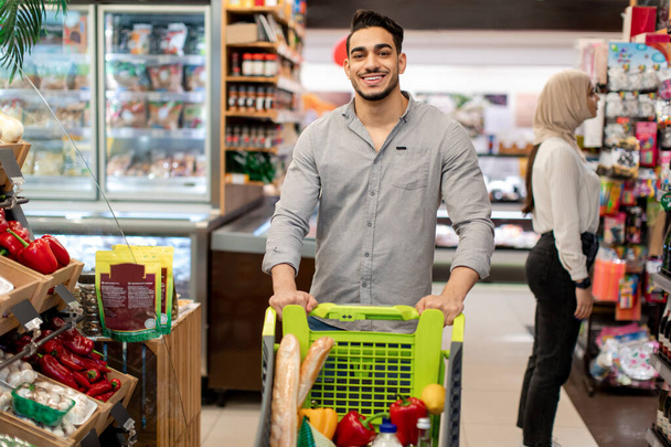 Vrolijke Egyptische Man doet kruidenierswinkel Wandelen In Moderne Supermarkt - Foto, afbeelding