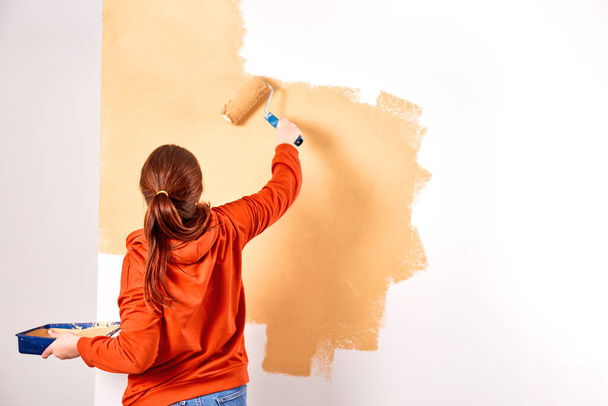 Mosolygó kaukázusi nő festi az otthonunk belső falát. Felújító lakás. javítási és felújítási koncepció. másolás helye - Fotó, kép