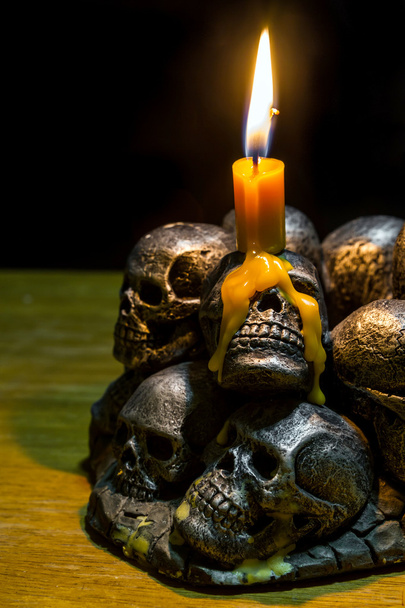 черепи зі свічкою, що горить на дерев'яному тлі в темряві
  - Фото, зображення