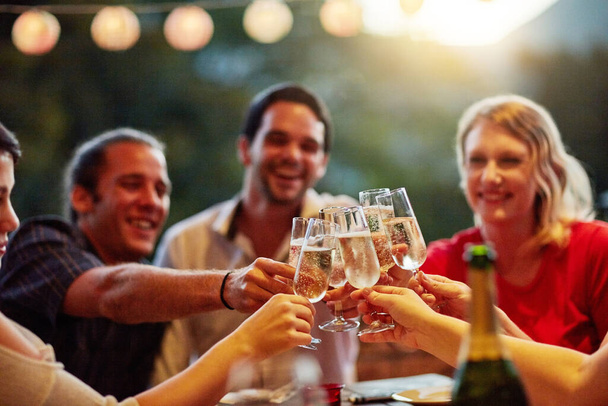 Goede tijden zijn om te vieren met vrienden. Shot van een groep gelukkige jonge vrienden toosten met champagne op een achtertuin diner feest. - Foto, afbeelding