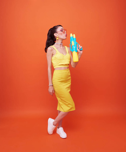 Jeune touriste heureuse avec pistolet à eau pendant Songkran festival studio de vacances tourné isolé sur fond orange. - Photo, image