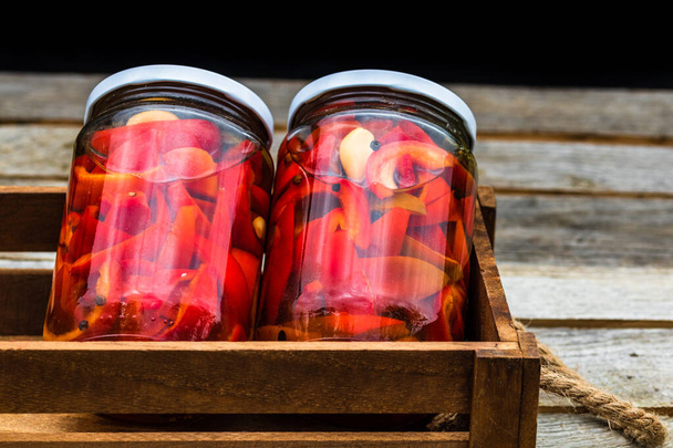 Caja de madera con frascos de vidrio con pimientos rojos en escabeche. Concepto de alimento conservado, verduras enlatadas aisladas en una composición rústica. - Foto, Imagen