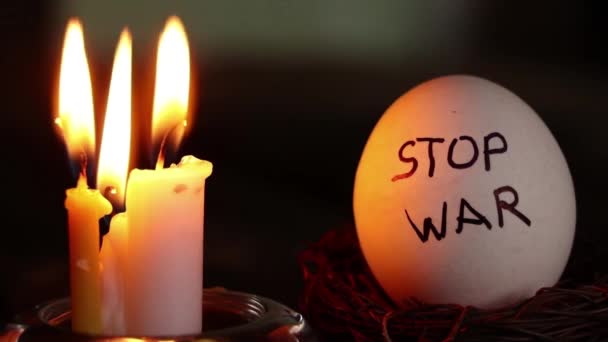 Stop válka je napsána na kuřecím bílém vejci, které leží vedle hořící svíčky ve tmě na Ukrajině, mír a kulturu - Záběry, video