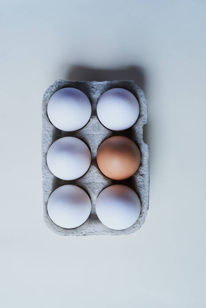 Будь винятком. Студійний знімок коробки на сірому фоні, що містить півдюжини яєць з одним яйцем, відмінним від решти
. - Фото, зображення