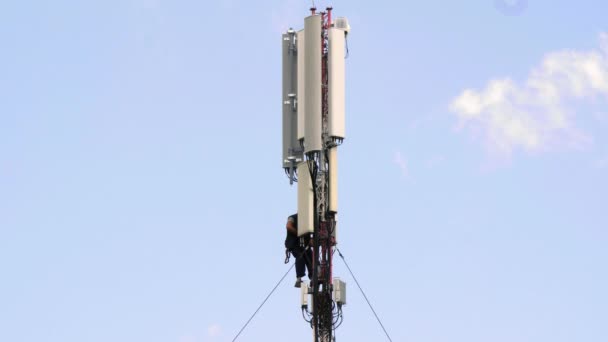 Riparatore elettricista ripara un'antenna di comunicazione mobile. Torre cellulare tra nuvole blu. Lavori di riparazione per ripristinare la connessione internet wireless e le comunicazioni mobili in alta quota. Apparecchiature elettroniche - Filmati, video