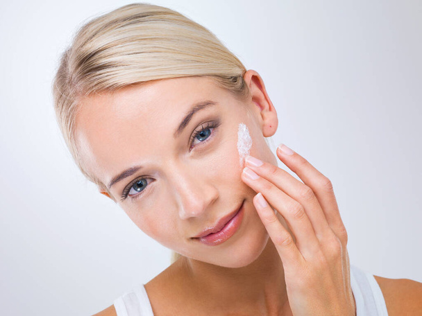For luxuriously soft skin.... A beautiful young woman applying moisturiser to her face. - Photo, Image