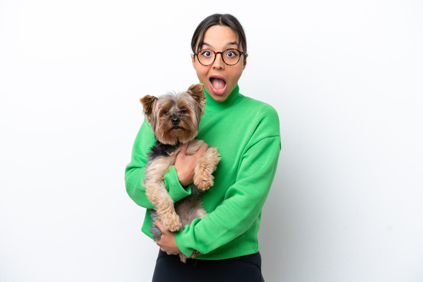 Young hispanic woman holding a dog isolated on white background with surprise and shocked facial expression - Photo, Image