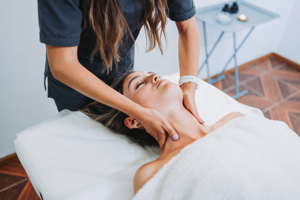 Terapeuta haciendo un masaje en el cuello a una paciente mujer boca arriba. Spa centro de bienestar. Cuidado de la piel. - Foto, Imagen