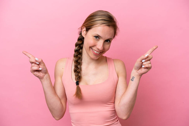 Mujer joven caucásica aislada sobre fondo rosa señalando el dedo a los laterales y feliz - Foto, imagen