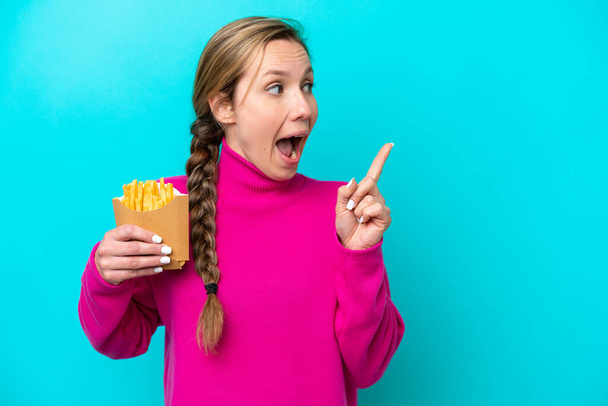 Young caucasian woman holding fried chips isolated on blue background intending to realizes the solution while lifting a finger up - Valokuva, kuva