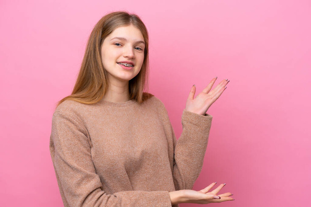 Teenager Russian girl isolated on pink background extending hands to the side for inviting to come - Fotografie, Obrázek