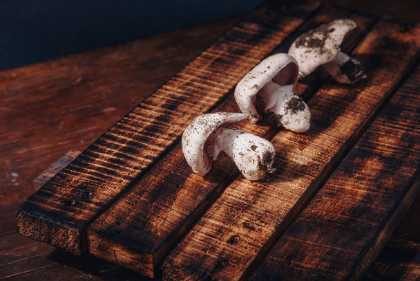 Fresh unwashed forest champignons on wooden kitchen board. Seasonal autumn mushrooms, tasty vegetarian cuisine. Close up shot - Foto, Bild