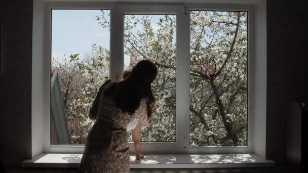 Ukrainische Mutter mit Baby nähert sich dem weißen Fenster. - Filmmaterial, Video