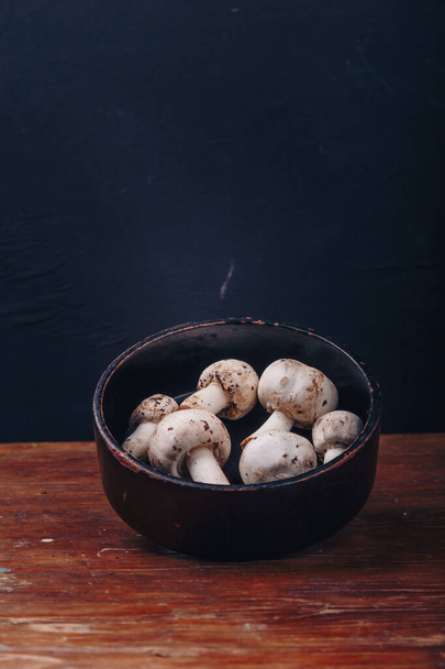 Νωπά ωμά μανιτάρια champignon σε μαύρο μπολ σε ξύλινο φόντο. Φθινοπωρινή συγκομιδή, εποχιακή βιολογική τροφή, υγιεινή διατροφή. Αντιγραφή χώρου, κατακόρυφος - Φωτογραφία, εικόνα