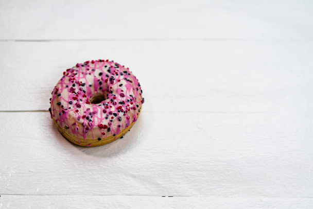 Colorful donuts on white wooden table. Sweet icing sugar food with glazed sprinkles, doughnut with frosting. Top view with copy space - Photo, Image