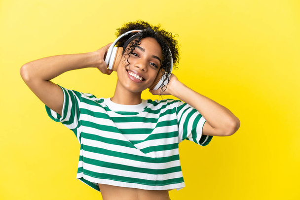 若いアフリカ系アメリカ人女性が黄色の背景で孤立｜リスニング音楽 - 写真・画像
