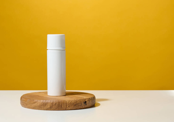 tubo redondo de plástico blanco para cosméticos, cremas y geles líquidos sobre un podio de madera, fondo amarillo - Foto, Imagen