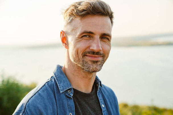 Grey european man smiling and looking at camera while standing outdoors - Фото, зображення