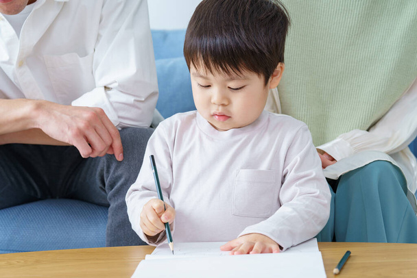 Ein Junge beim Zeichnen mit dem Bleistift und seine Eltern, die darüber wachen - Foto, Bild