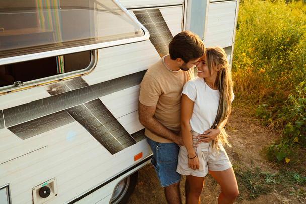 White couple hugging and smiling while standing by trailer outdoors - Φωτογραφία, εικόνα