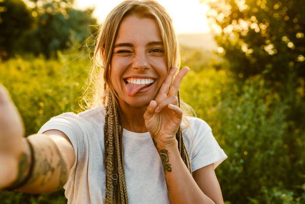 White young woman showing her tongue while taking selfie photo outdoors - Foto, Imagem
