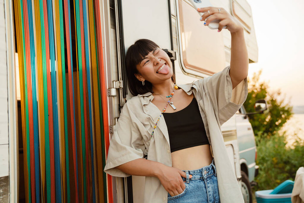 Asian young woman taking selfie on cellphone by trailer outdoors - Foto, Imagem