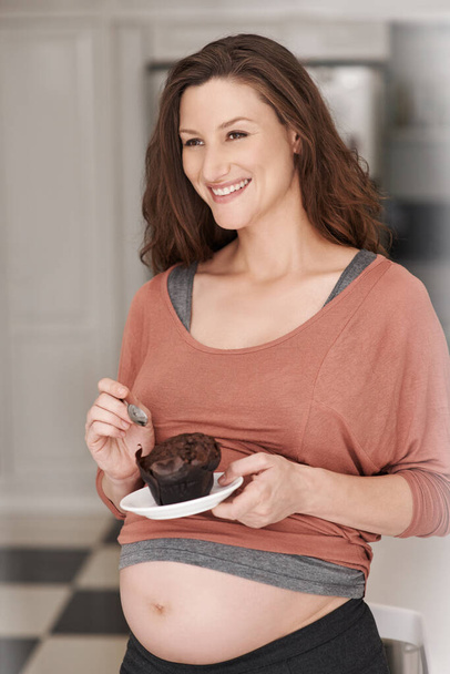 Těhotenské touhy. Vystřižený záběr mladé těhotné ženy jíst cupcake v kuchyni. - Fotografie, Obrázek