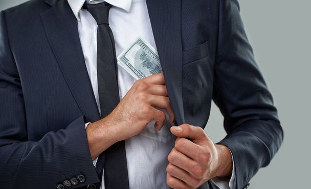 Os verdadeiros criminosos usam ternos, não balaclavas... imagem cortada de um homem de negócios colocando dinheiro em seu bolso. - Foto, Imagem