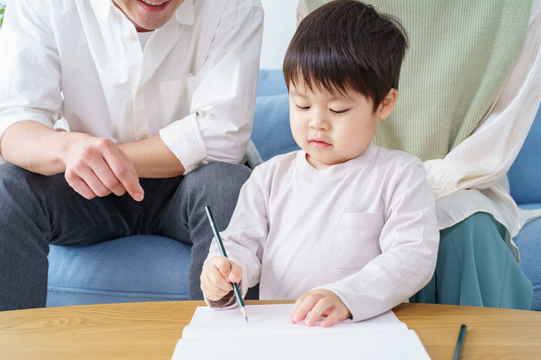 Een jongen die met een potlood aan het tekenen is en zijn ouders die er over waken - Foto, afbeelding