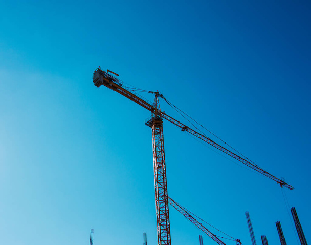 High-rise construction crane with a long yellow boom against the blue sky. - Photo, Image