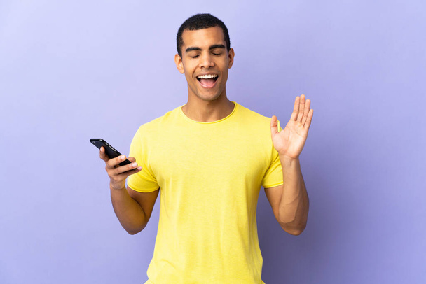 African American man over isolated purple background using mobile phone laughing - Foto, imagen