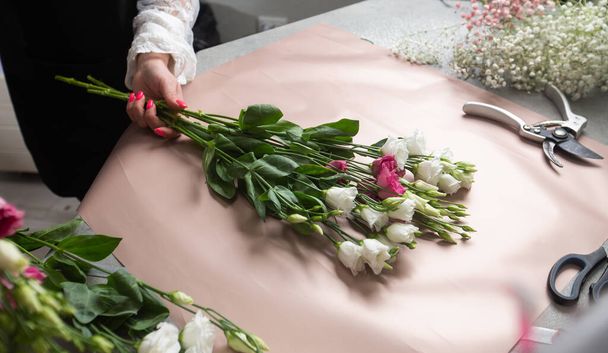 a female florist wrapping beautiful bouquet with paper at table, top view on the desktop. High quality photo - Foto, afbeelding