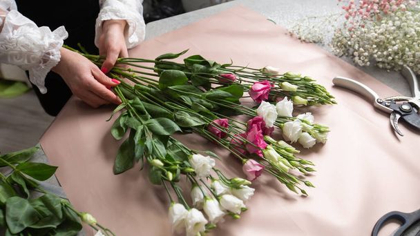 a female florist wrapping beautiful bouquet with paper at table, top view on the desktop. High quality photo - Fotoğraf, Görsel